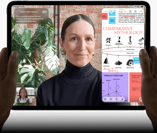 Asztrofekete iPad Pro szemből, fekvő tájolásban, lekerekített sarkokkal, fekete kijelzőkerettel. A bal és jobb szélén
      egy-egy kéz fogja, a kijelzőn élőben fordított FaceTime-beszélgetés, valamint egy oktatási célú alkalmazás jelenik meg, amely
      egy komparatív mitológiáról szóló prezentációt tartalmaz szöveggel, ábrákkal és kézzel írt jegyzetekkel