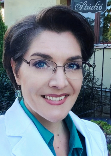 Közeli portré egy rövid hajú, szemüveges, mosolygós nőről világos kabátban. Nő, mosoly,  szakember, portré.